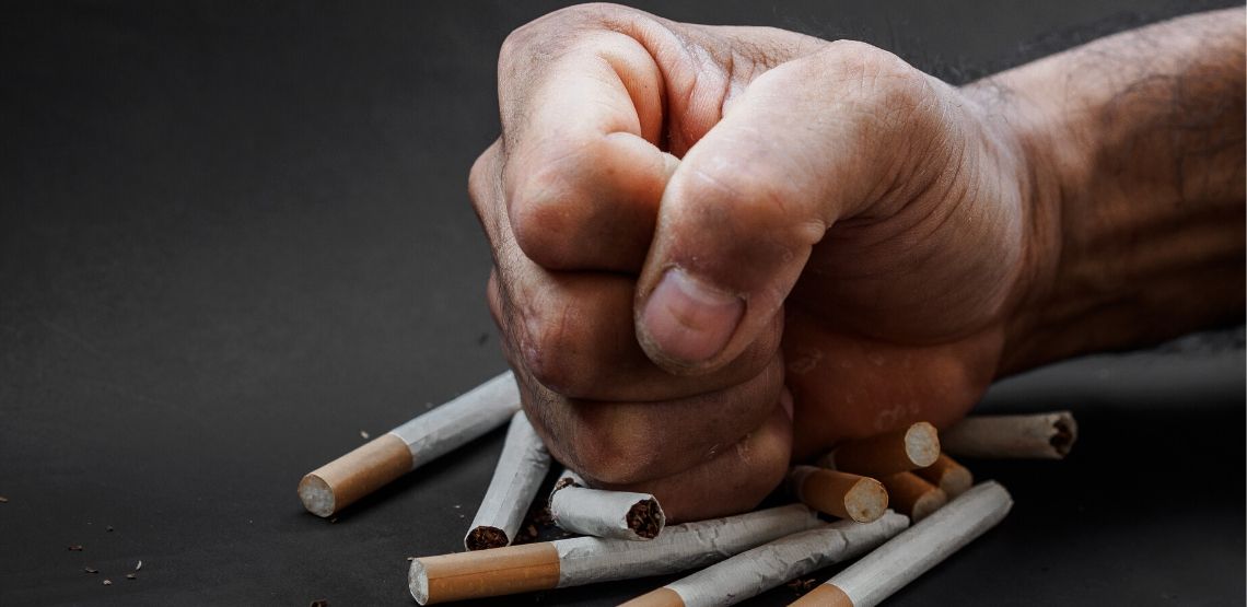 man crushing a bunch of cigarettes with his fist