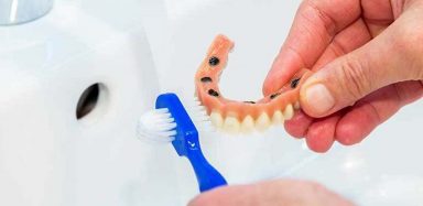 A person cleaning a pair of dentures with a soft brush.