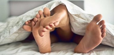 People's feet on top of each other, under bed covers