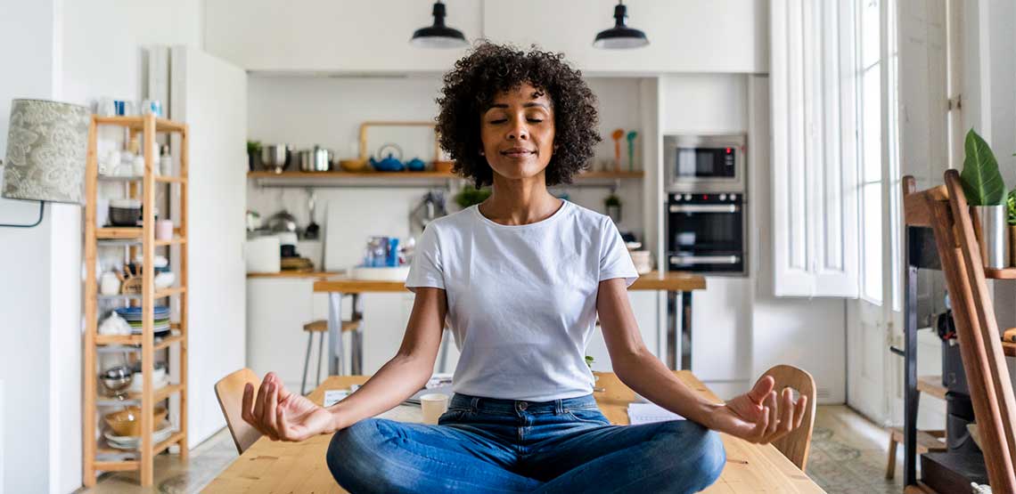 a woman sitting crossed legged on her kitchen table while meditating for mindfulness based stress reduction