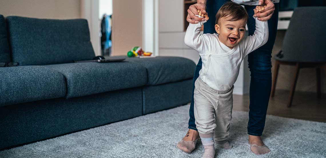 A toddler learning how to walk with its parent holding its hands