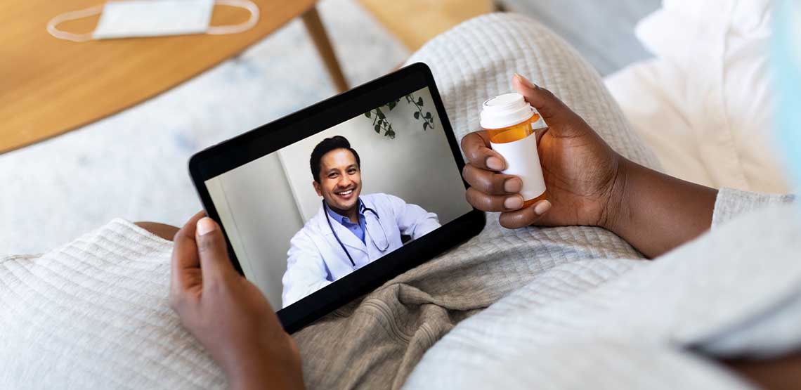 A person holding their tablet and medicine during a virtual doctor appointment on their tablet.