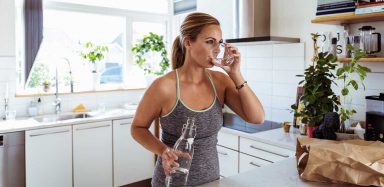 A woman standing in her kitchen drinking a glass of water