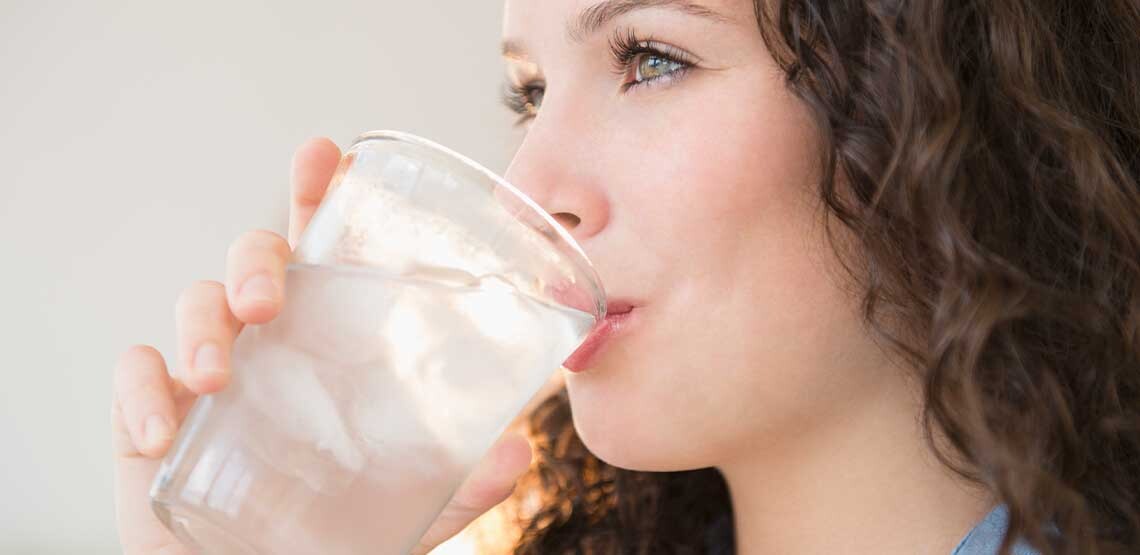 A side view headshot of a Caucasian woman with brown hair drinking a glass of water.