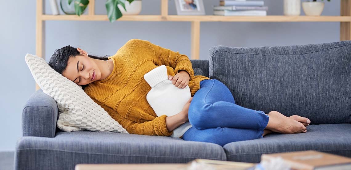 A woman laying on a couch with a hot water bottle.