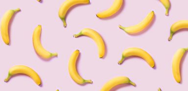 Multiple bananas laying on a pink background