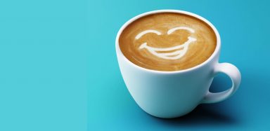 A mug of coffee on a blue background with latte art of a smile